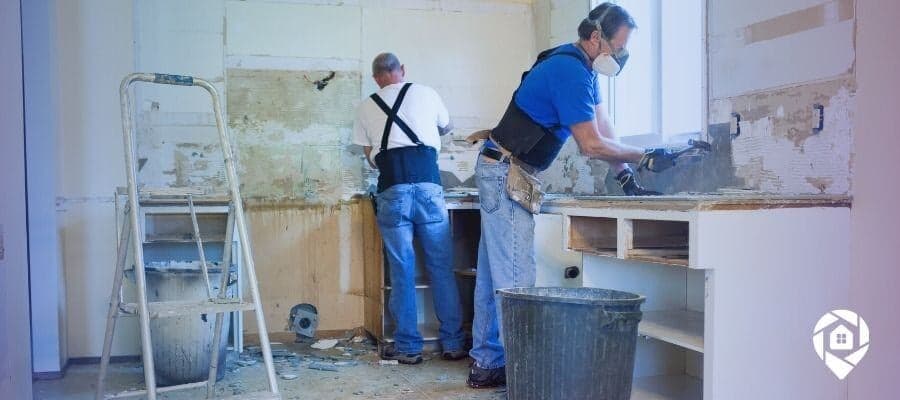 Two contractors renovating a kitchen, removing old cabinets and preparing for upgrades.