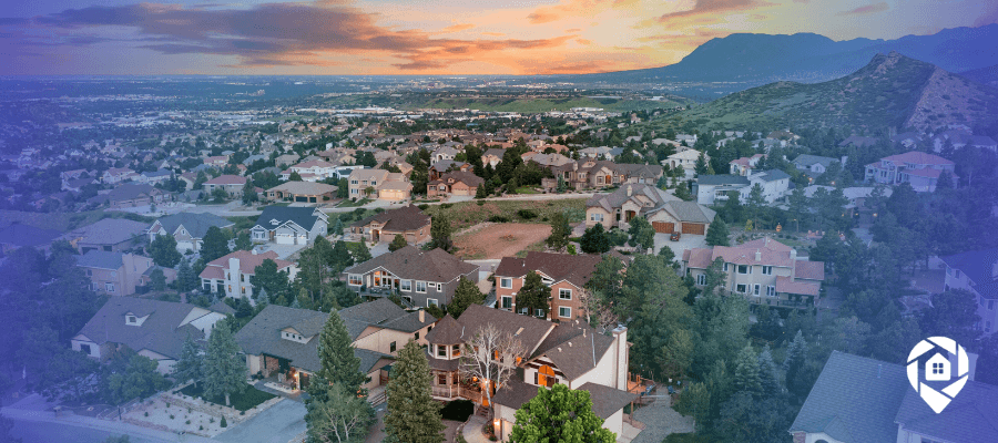 Aerial drone view of a hillside suburban neighborhood at sunset with mountains in the distance.