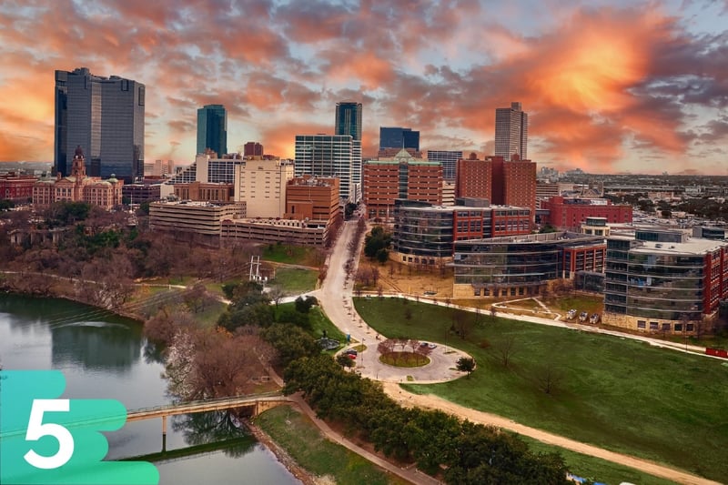 Sunset aerial shot of downtown Fort Worth, Texas, with a waterfront park up front and the buildings toward the back.