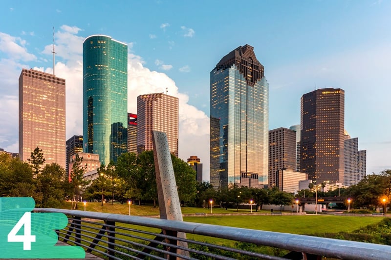 Ground shot from a Houston park featuring the large skyscrapers in the back on a backdrop of a blue partly cloudy day.