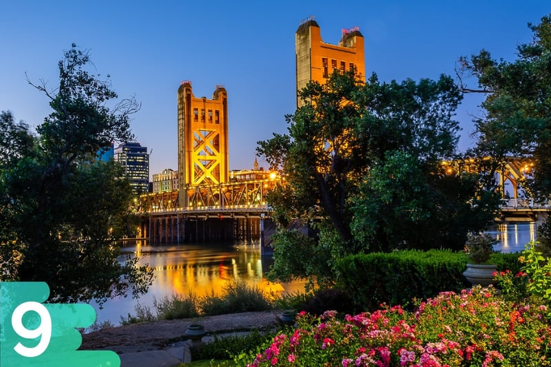 Flower garden in Sacramento with large lit-up bridge in the background leading into downtown Sacramento.