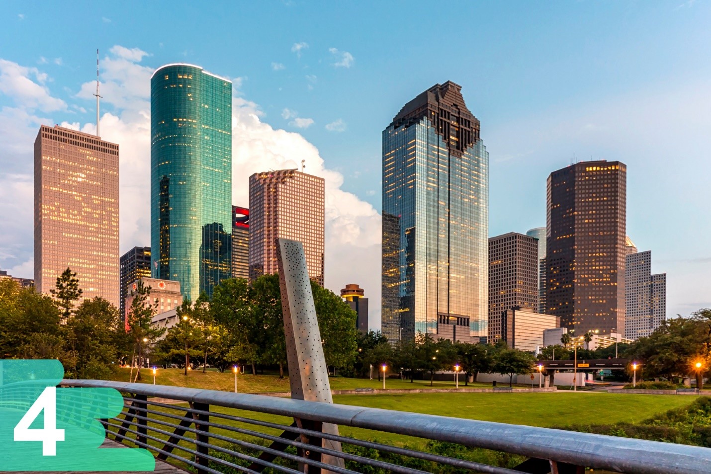 Ground shot from a Houston park featuring the large skyscrapers in the back on a backdrop of a blue partly cloudy day.
